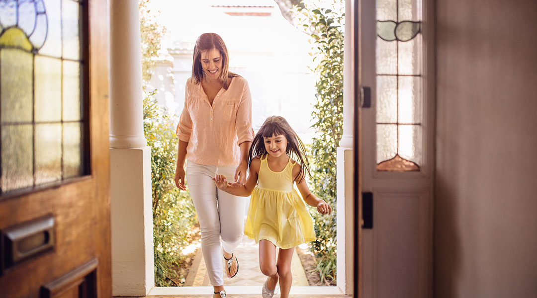 a mother and daughter smiling and running through the door of a house