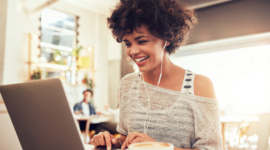 A young women with curly hair, smiling as she works on her laptop